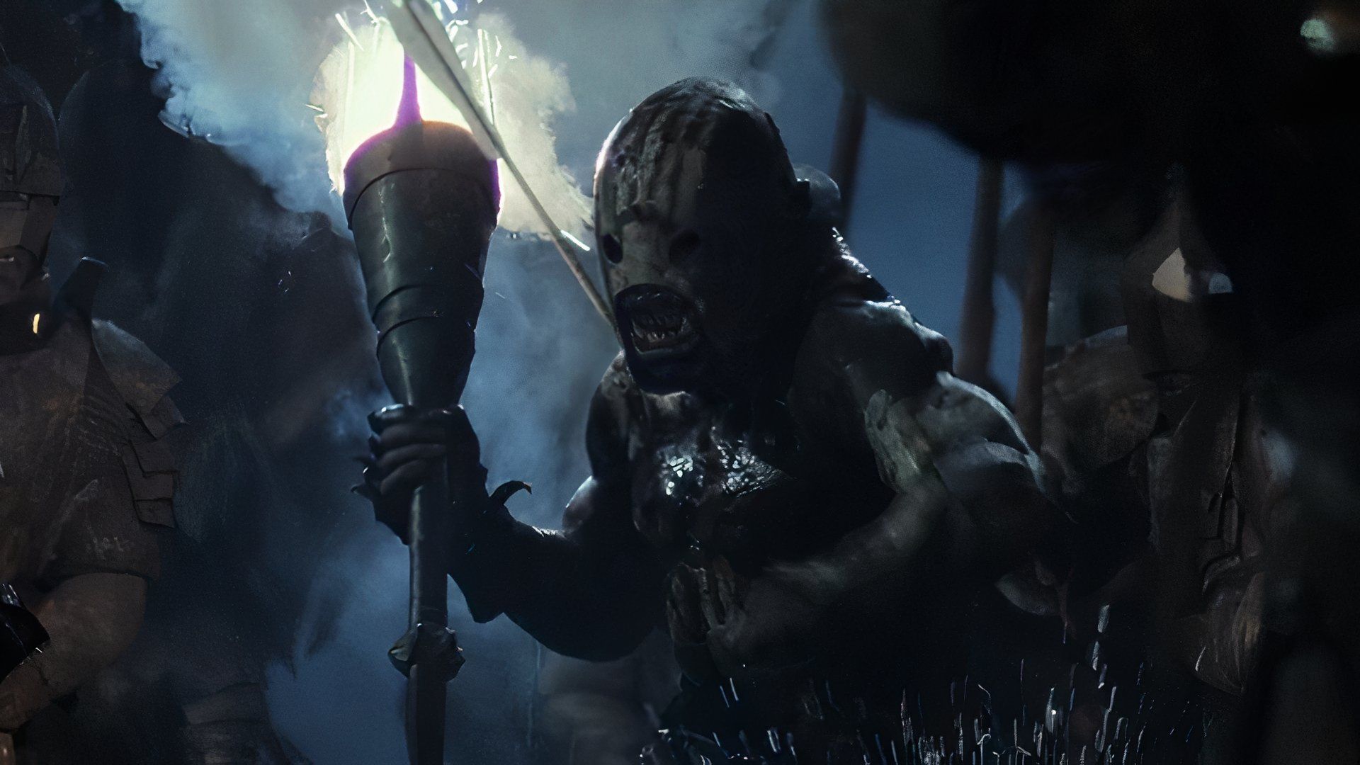 An Uruk-hai, holding a torch, charges forward in a scene from The Lord of the Rings: The Two Towers