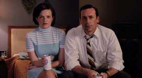Peggy and Don sitting on a bed together watching a TV with drinks in their hands on Mad Men