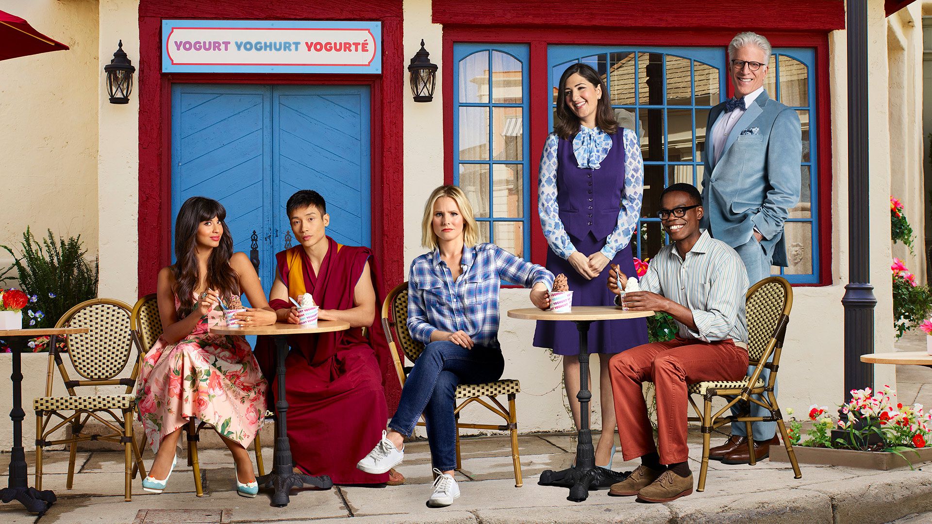 The cast of The Good Place sitting outside of a quaint store