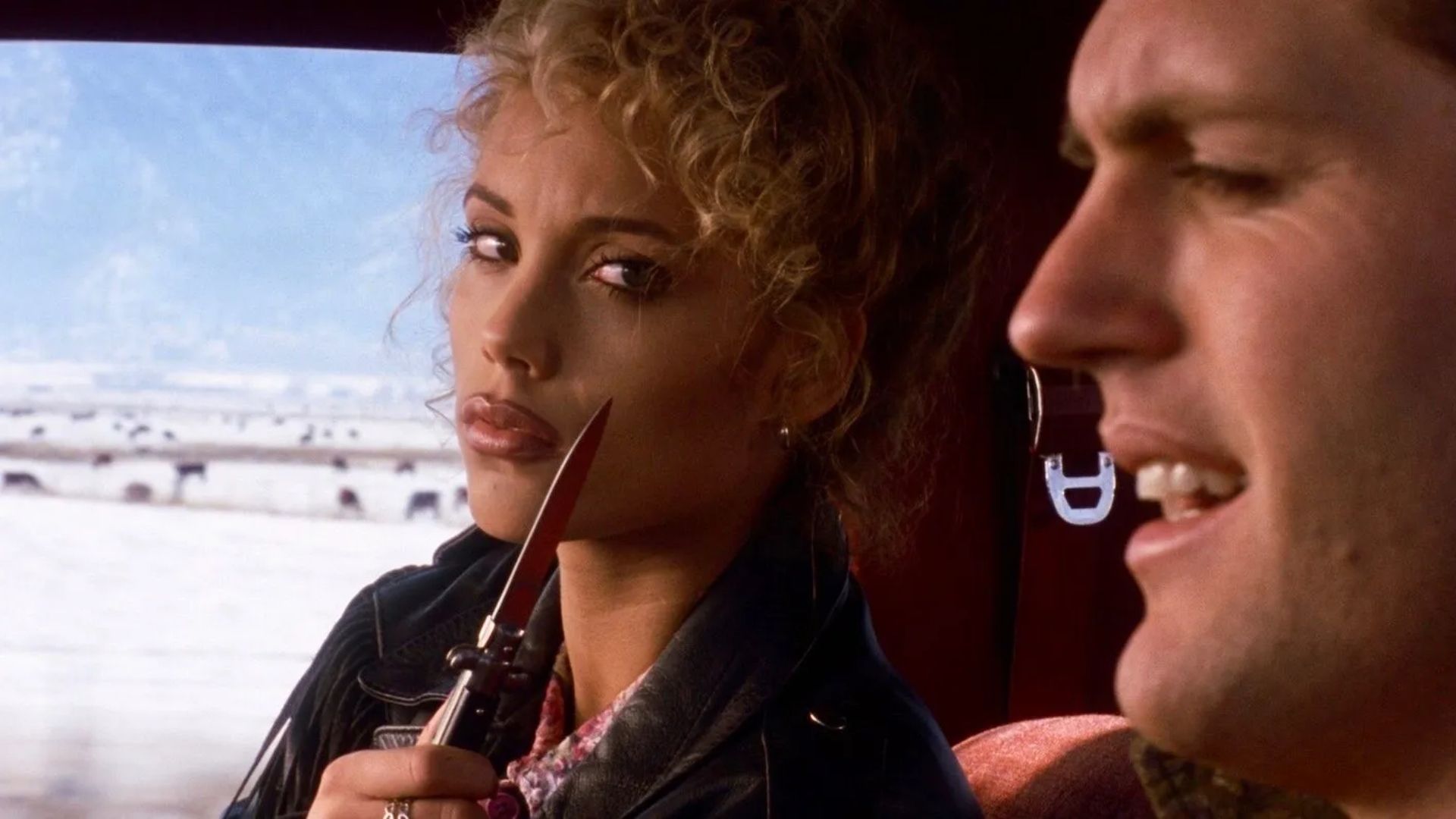 Elizabeth Berkley brandishing a knife in a car with a man as Nomi Malone in Showgirls