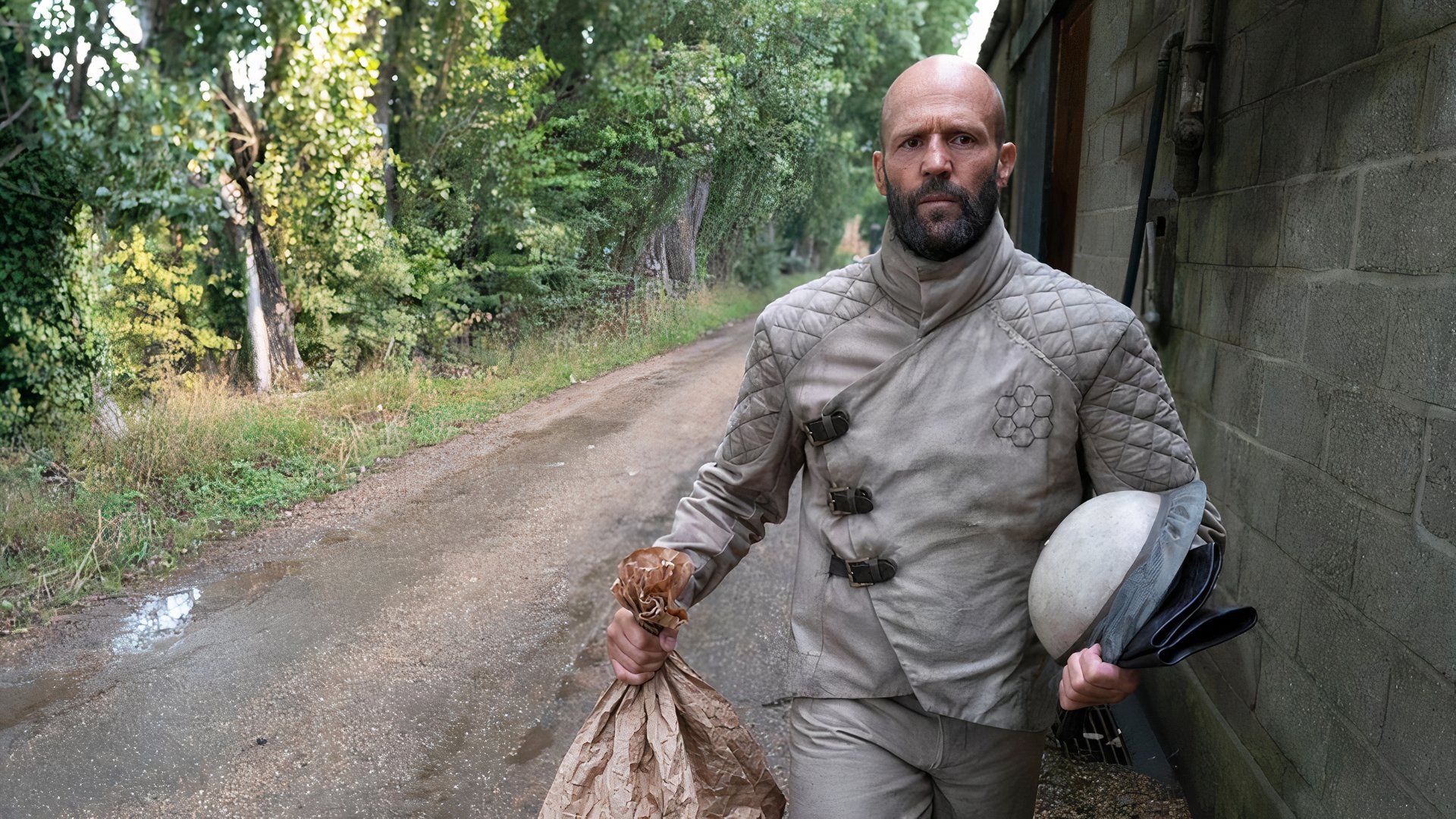 Jason Statham wears a beekeeping suit and walks holding a bag in the film the beekeeper