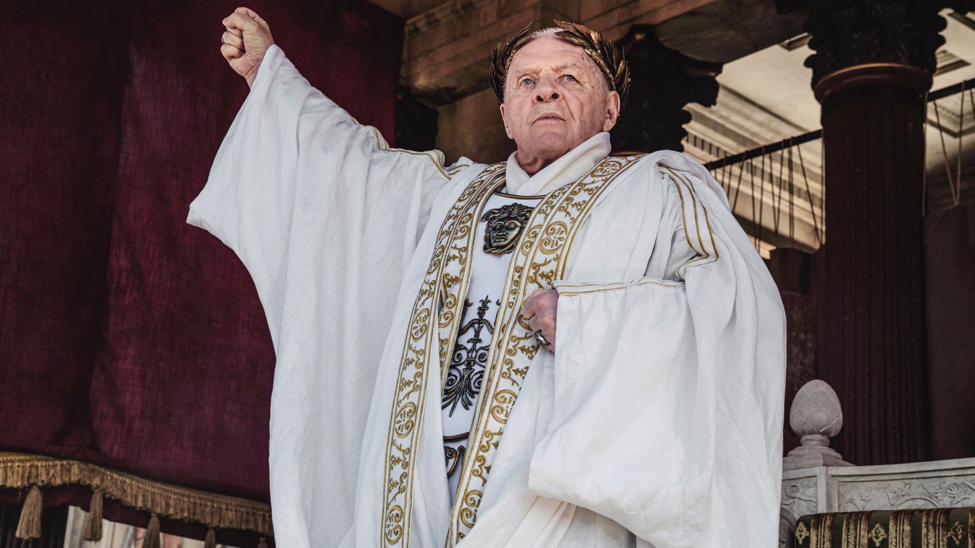 Anthony Hopkins raising his fist while wearing white robes in Those About to Die