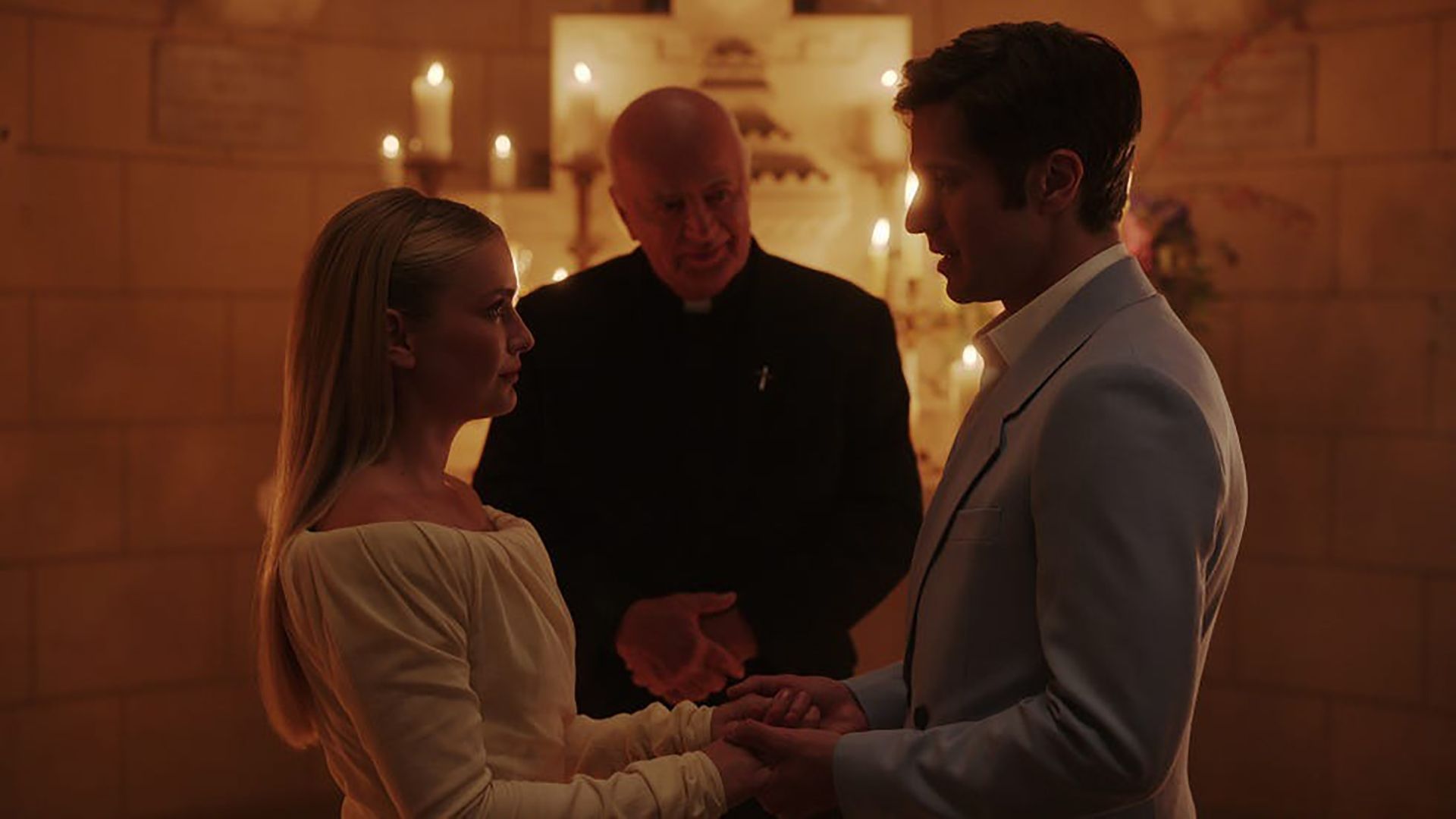 Camille and Gabriel holding hands in front of a priest on Emily in Paris