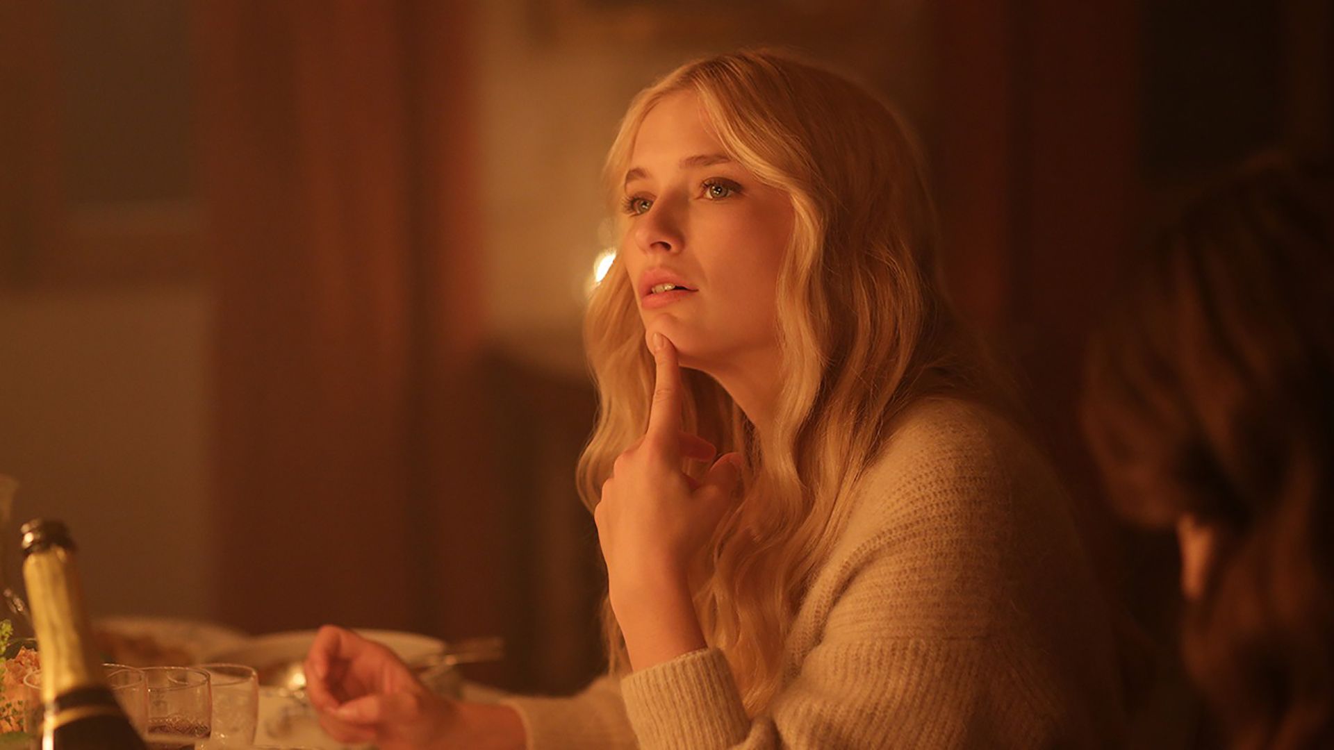 Emily at a dinner table lit by candles with her finger on her chin looking pensive on Emily in Paris.