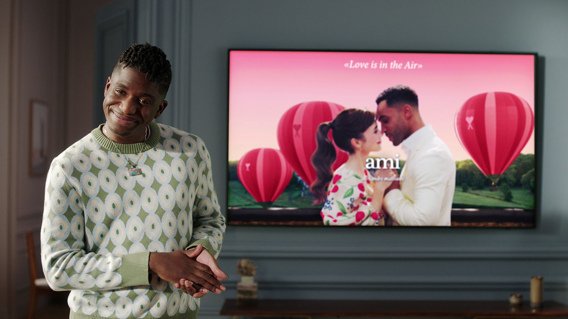 Julien standing in front of a screen showing an image of Emily and Alfie in a romantic campaign on Emily in Paris