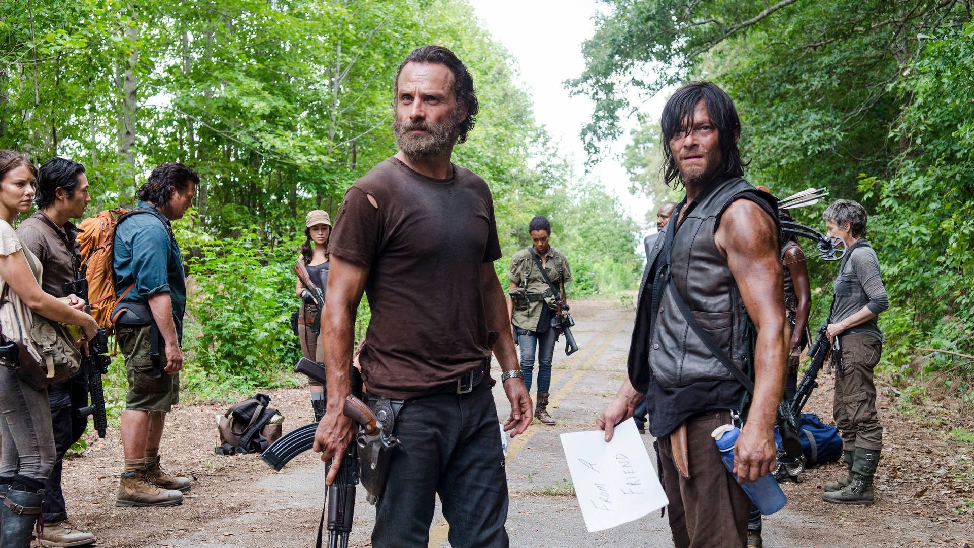 Rick and Daryl standing on the road looking at something, others behind them on The Walking Dead