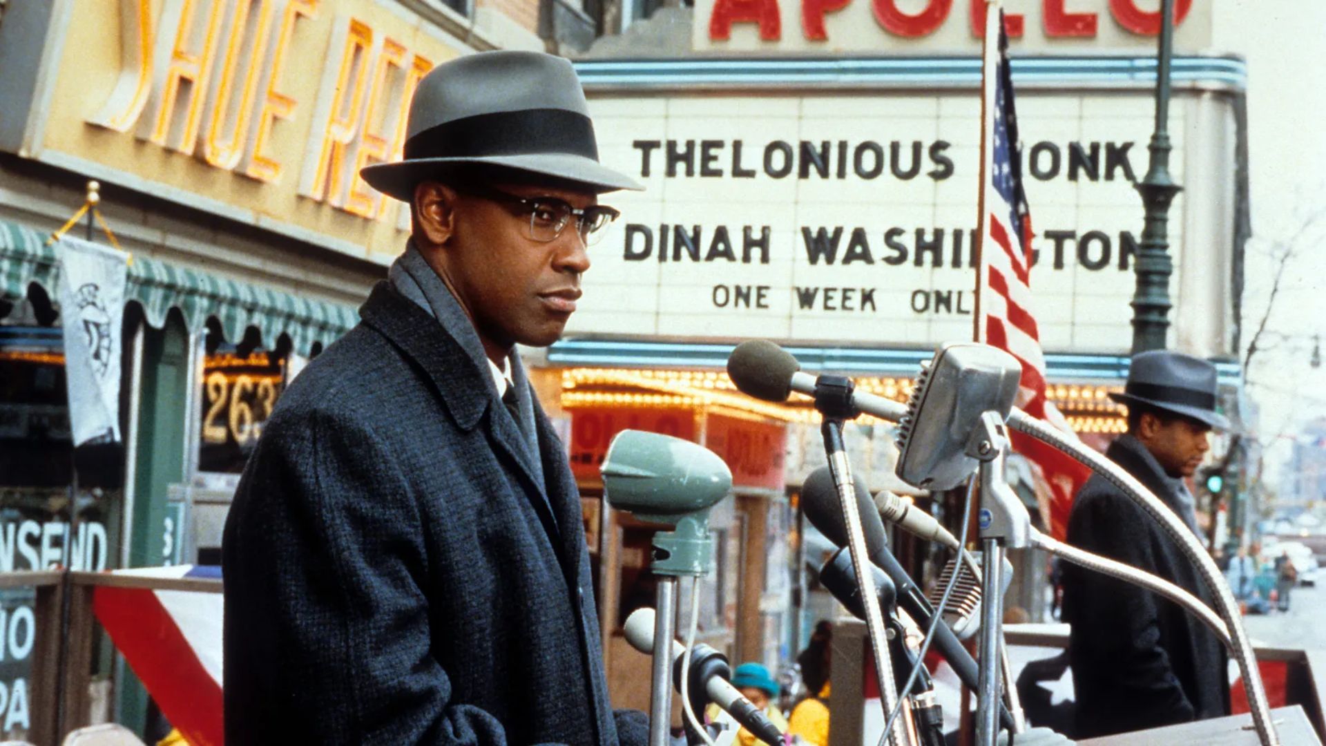 Denzel Washington at a press podium by the American flag in the movie Malcolm X