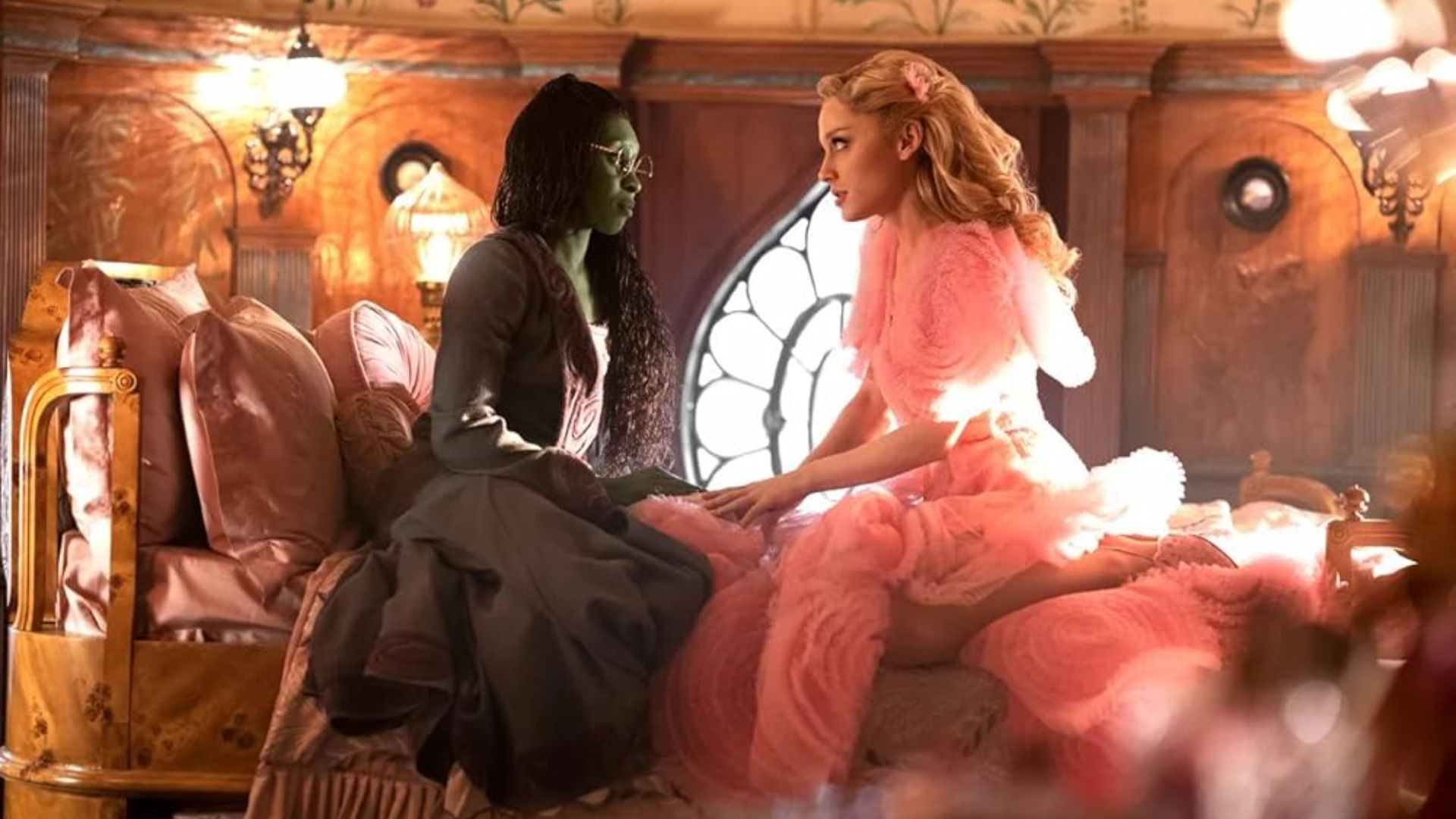 Cynthia Erivo and Ariana Grande sit on a bed together in Wicked