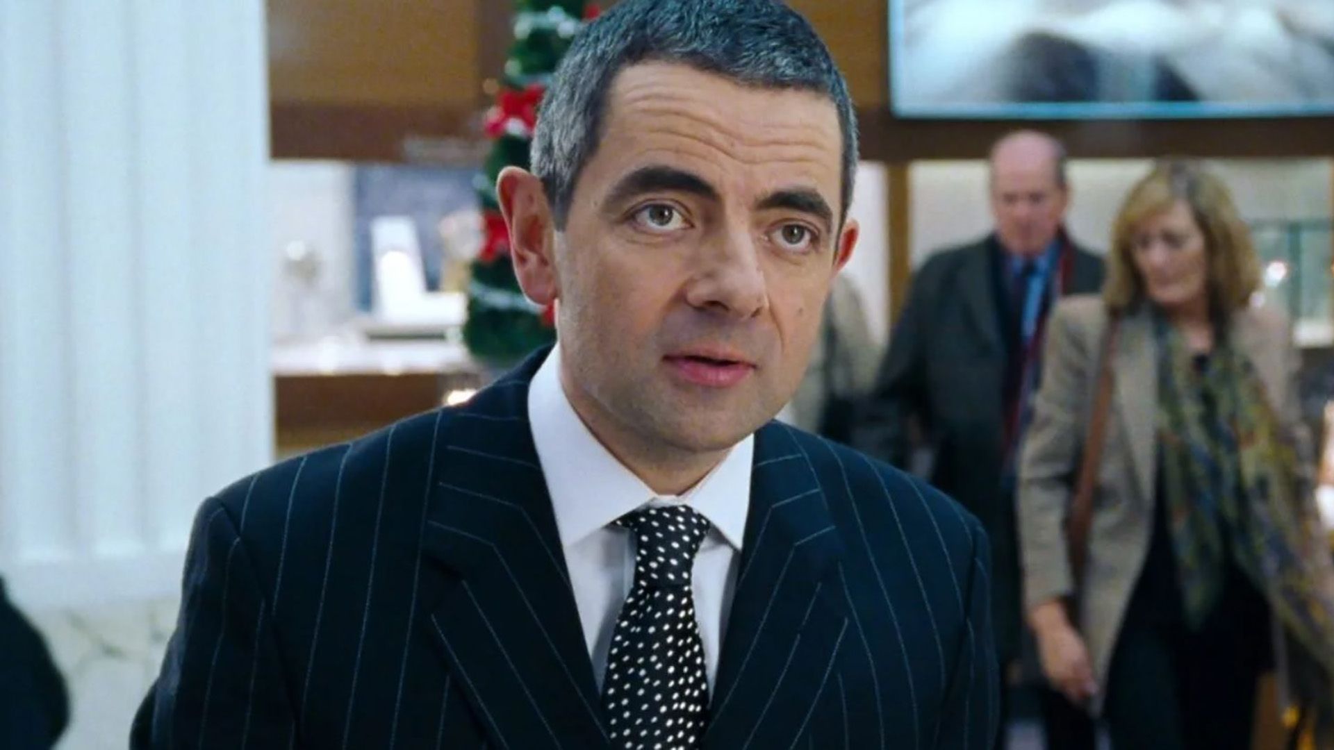 Rowan Atkinson as Rufus in a suit behind the jewelry counter in Love Actually