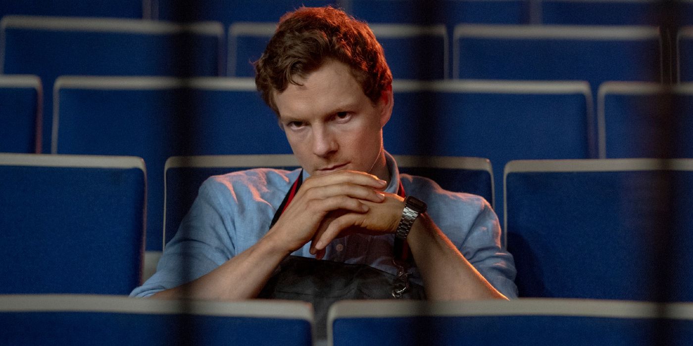 Dexter sitting in an auditorium, hands to his chin smiling wickedly in Dexter: Original Sin.