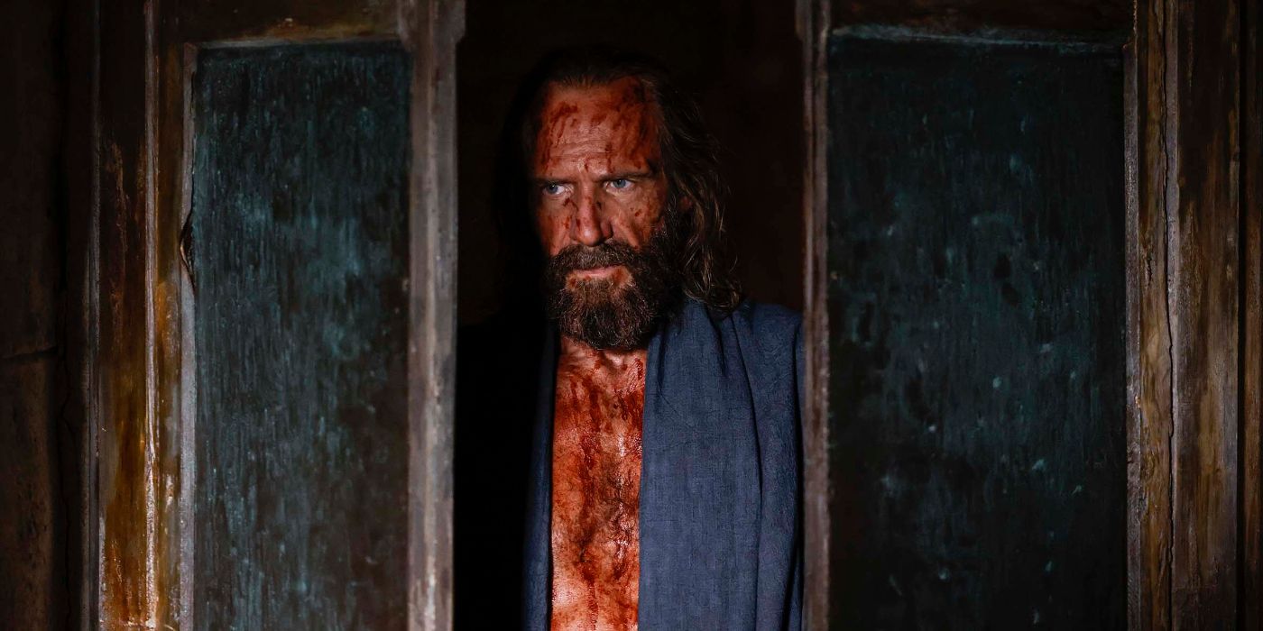 Ralph Fiennes as Odysseus covered in blood in a doorway in the 2024 movie The Return