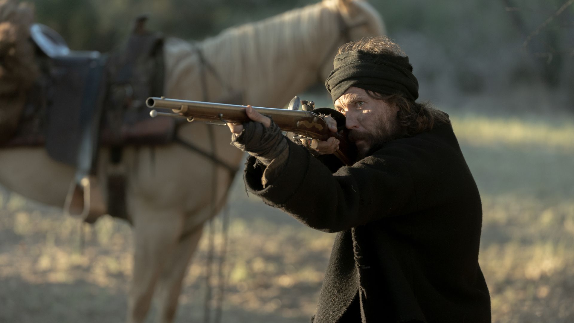 Taylor Kitsch points a rifle by his horse in the Netflix Western series American Primeval