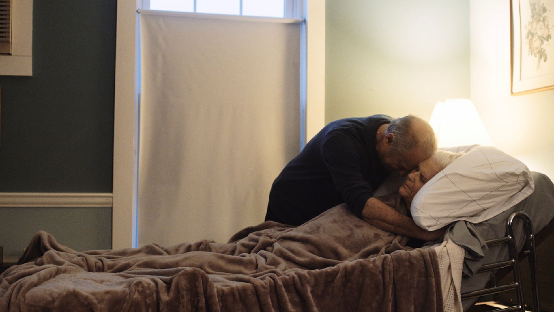 A man hugs a dying woman in bed in the movie Other Side