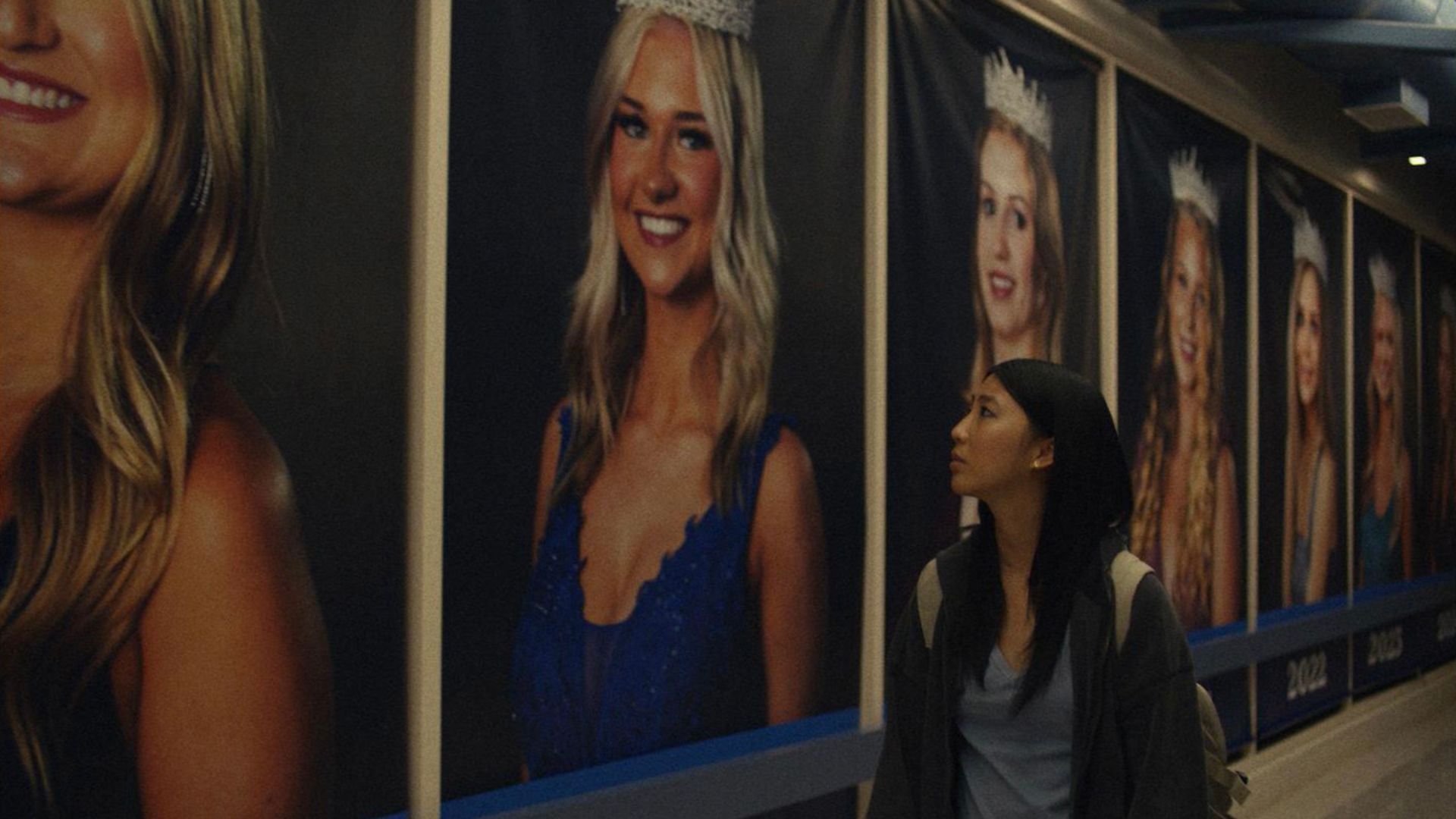 An Asian girl looks at giant posters of blonde homecoming queens in the movie Slanted