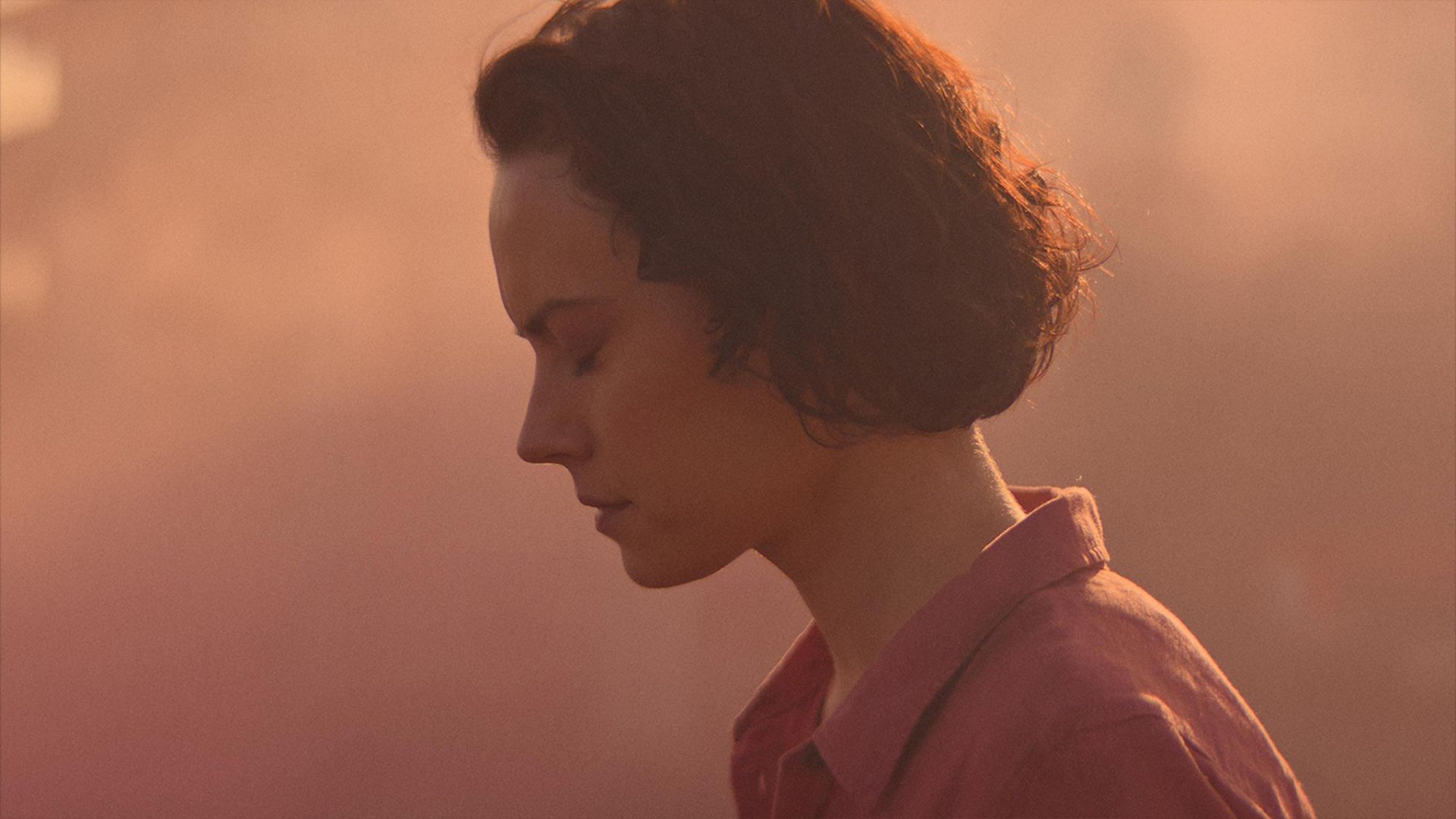 Daisy Ridley shuts her eyes in an orange haze in the movie We Bury the Dead