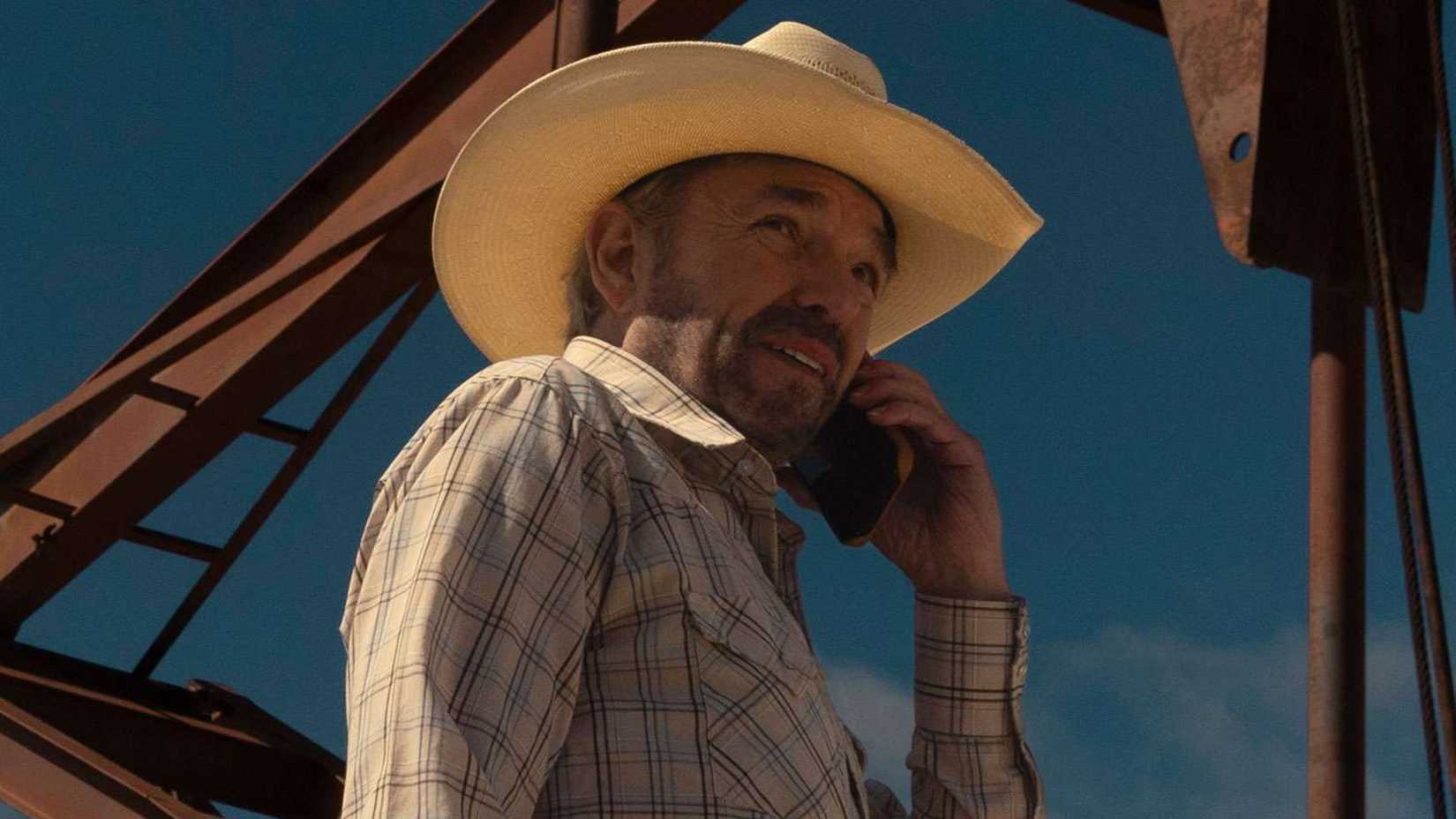 Tommy talks on the phone under an oil derrick in Landman