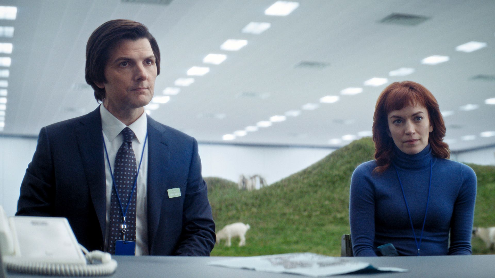 Mark and Helly sitting at a desk with grass in the background in Severance.