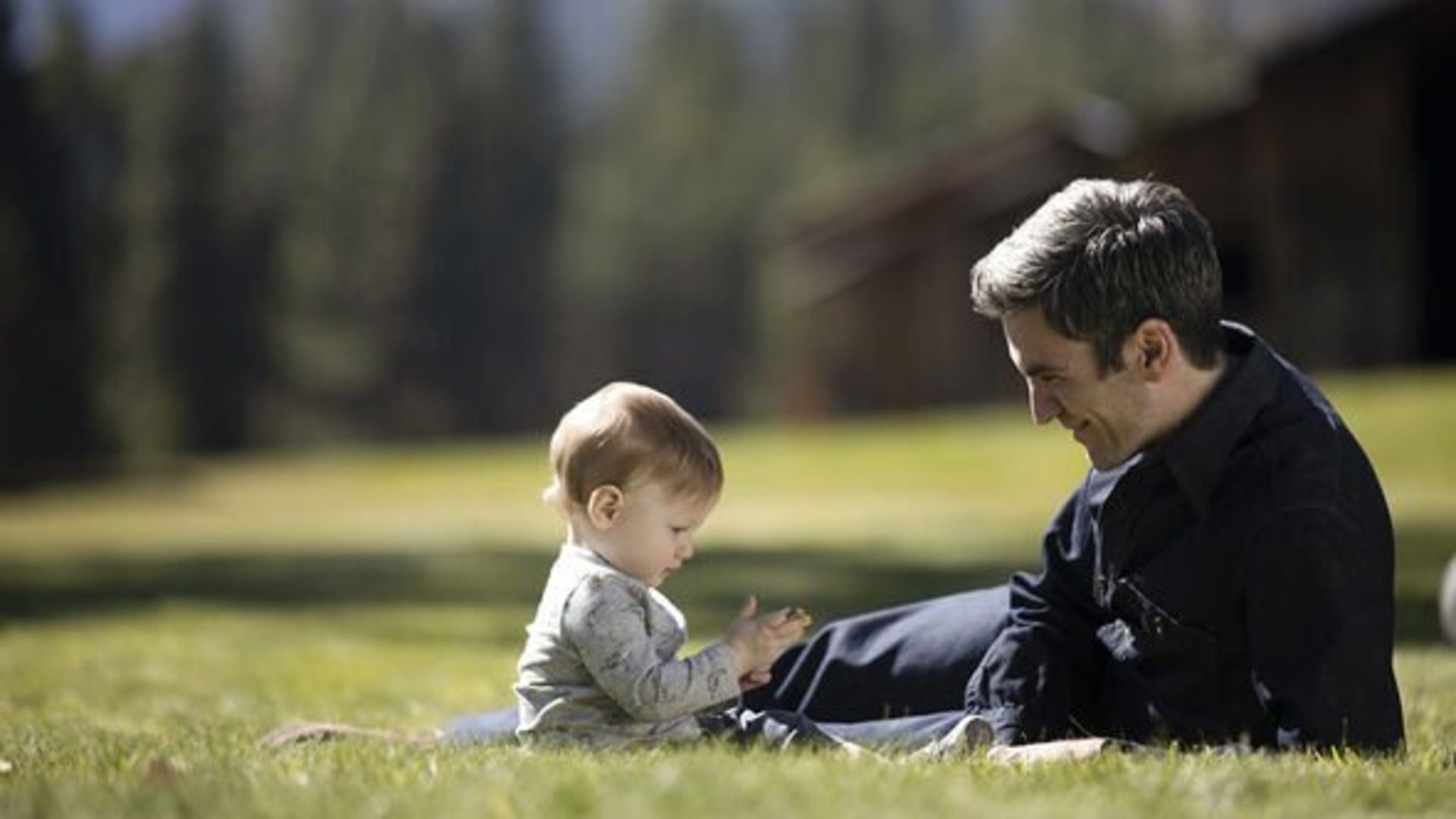 Jamie sits with his son in the grass in Yellowstone