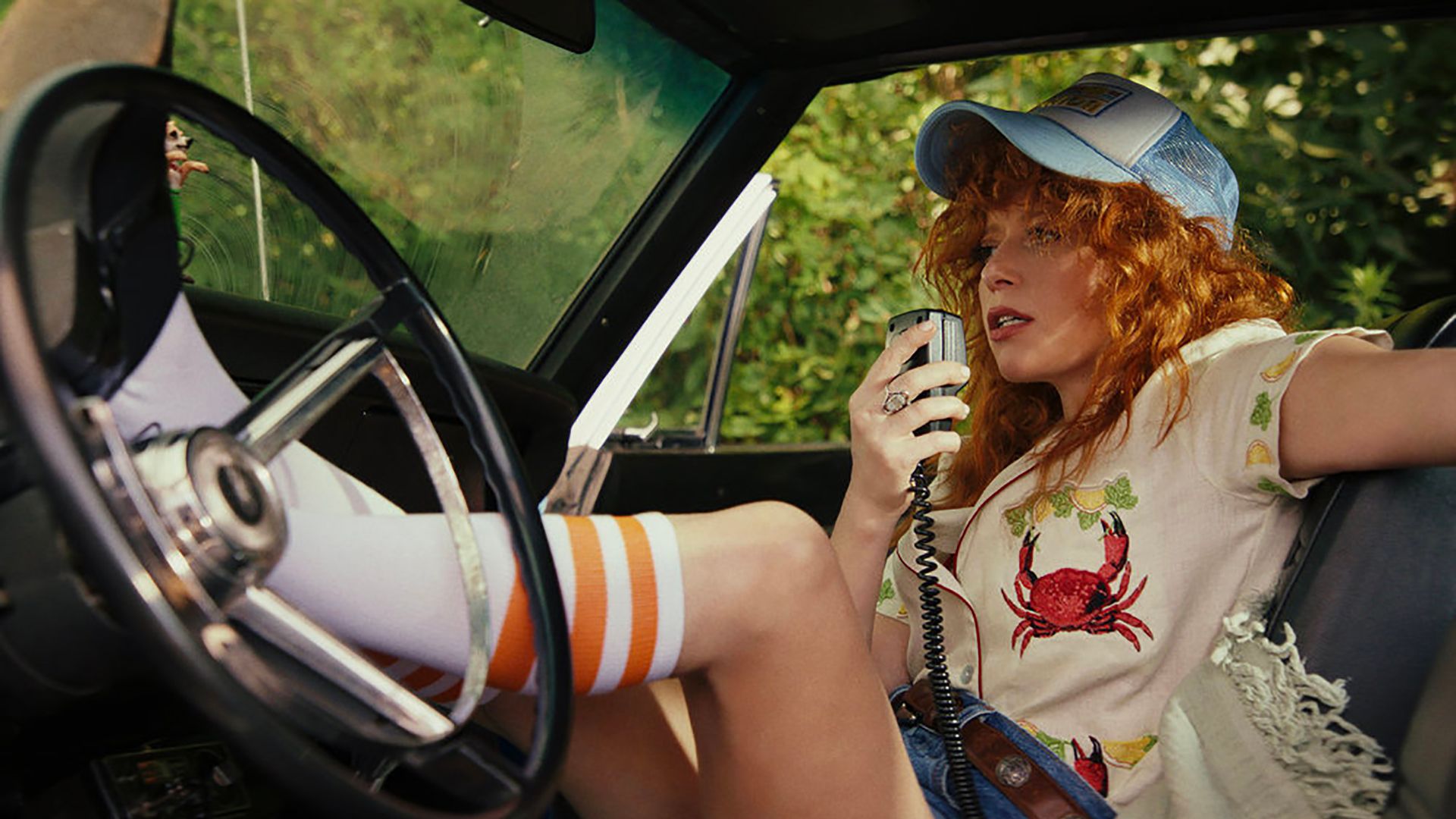 Charlie talking on a radio in the car with her leg up on the steering wheel in Poker Face.