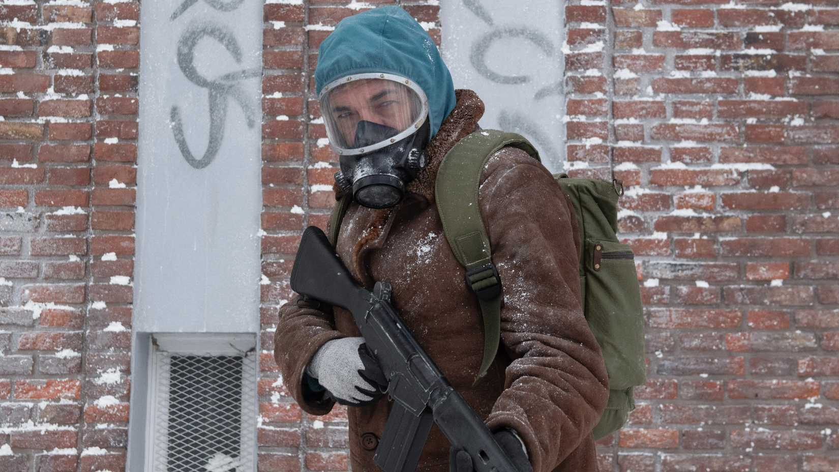 Juan holds a machine gun by a brick building in The Eternaut