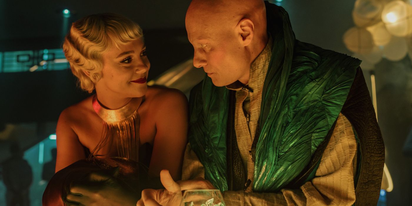 Synnove Karlsen as Bayta Mallow smiling as Tómas Lemarquis as Magnifico Giganticus at the bar in Foundation
