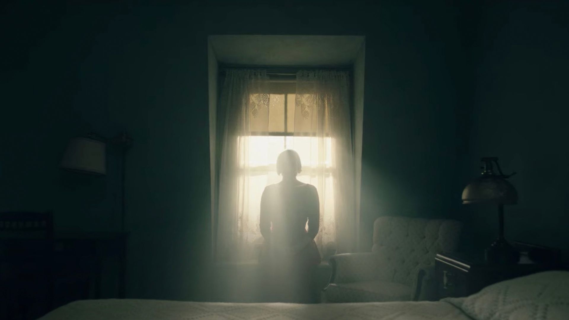 Offred sitting by the window in the dark in her room in The Handmaid's Tale.