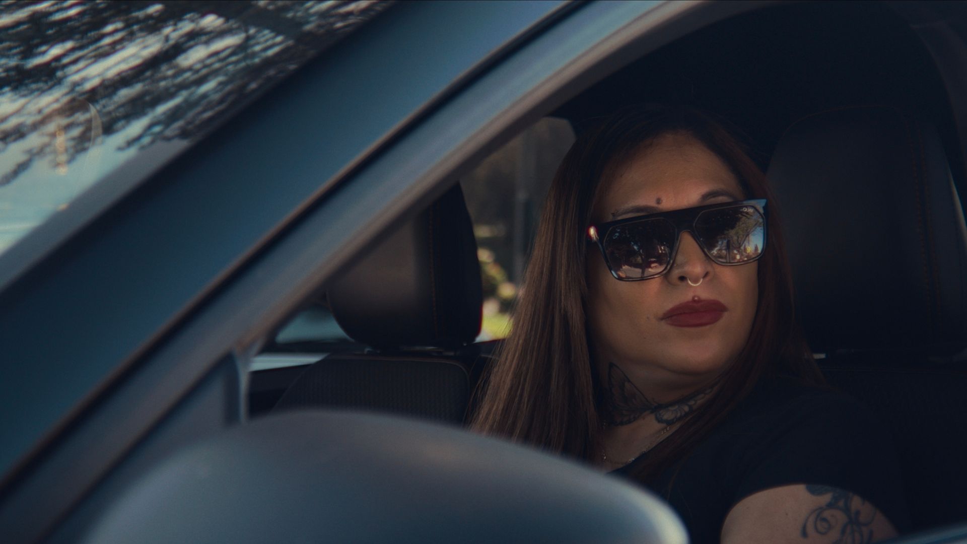 A woman wearing sunglasses sitting in her car in Trainwreck: P.I. Moms.