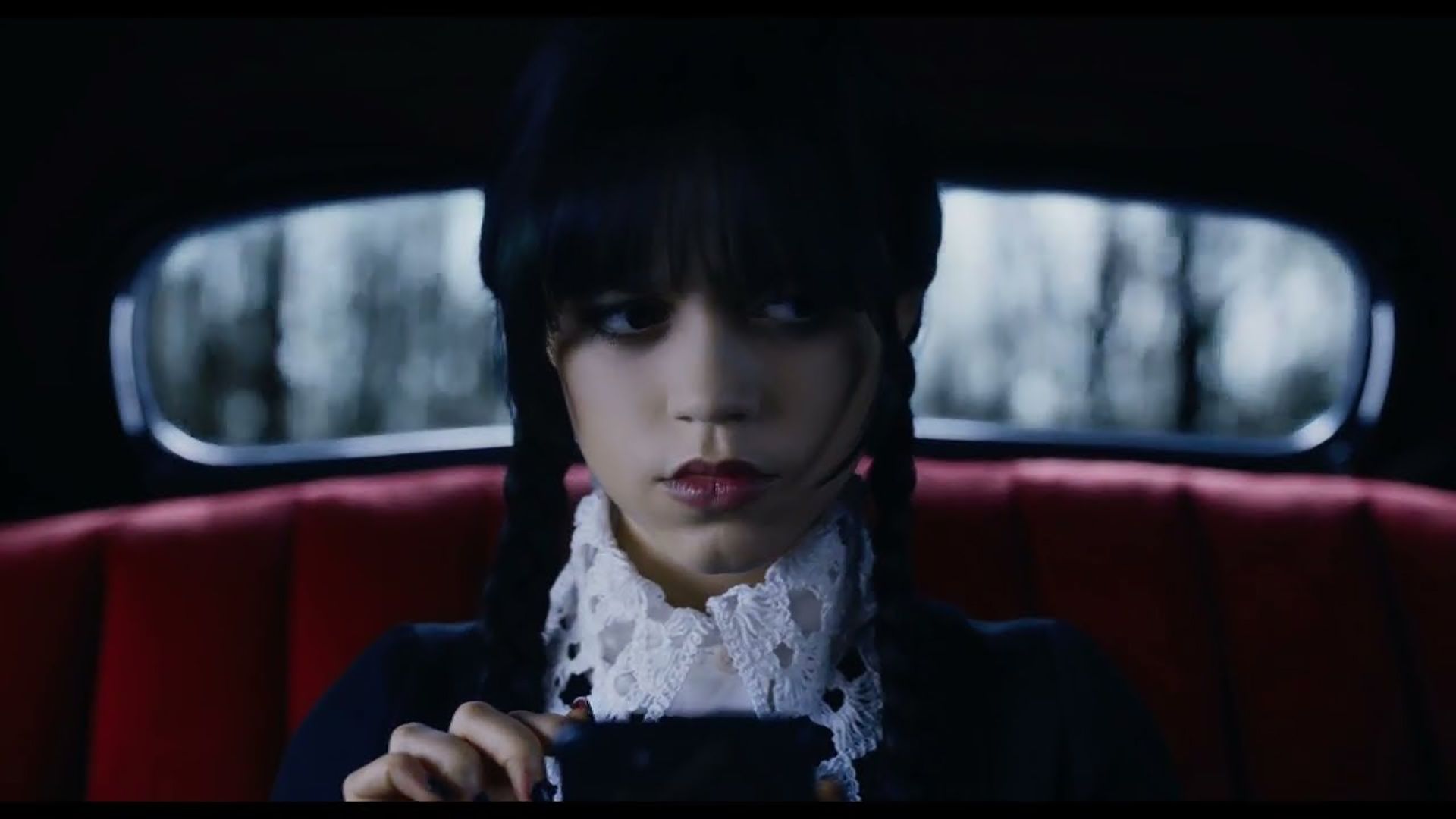 Wednesday in the car on her phone looking intrigued.