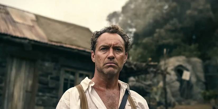 Jude Law in Eden standing outside near a small building wearing a white collared shirt