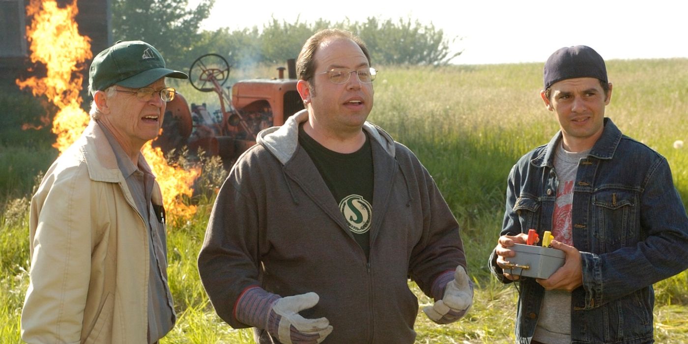 The cast of Corner Gas in front of a tractor on fire